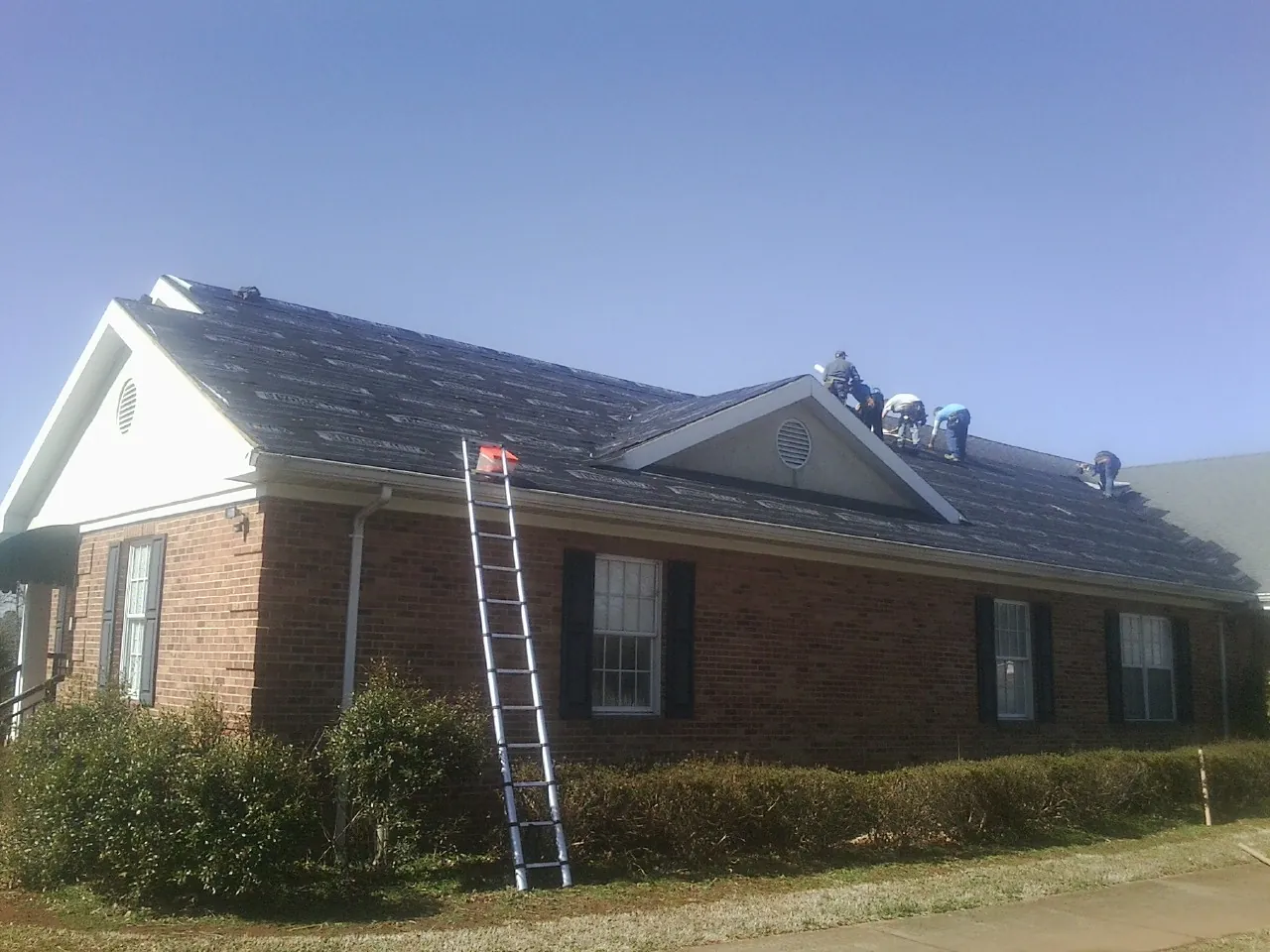 Crew tearing shingles off a brick ranch roof with a ladder set — Metal Roof Repair work by our crew in Inver Grove Heights
