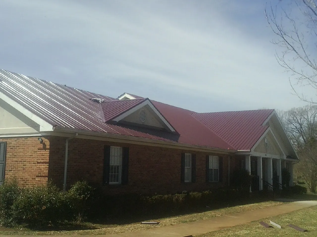 Red metal roof with gabled entries on a long brick building, from a Hail Damage Roof Repair job in Inver Grove Heights