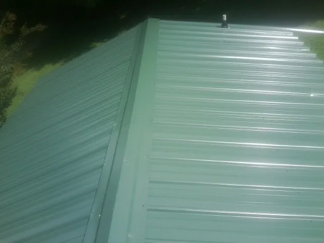 New green metal panels meeting at the ridge of a roof — Flat Roof Repair work by our crew in Inver Grove Heights