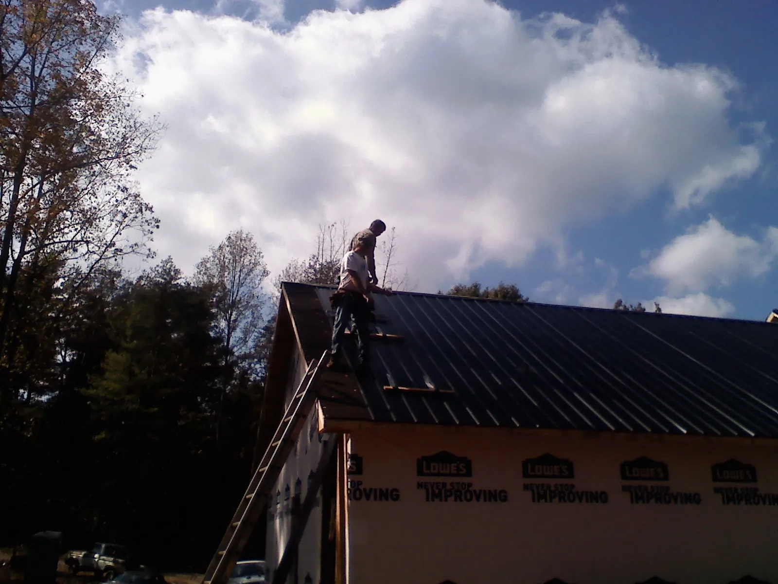 Roofer fastening dark metal panels high against a cloudy sky, from a Roof Inspection job in Inver Grove Heights