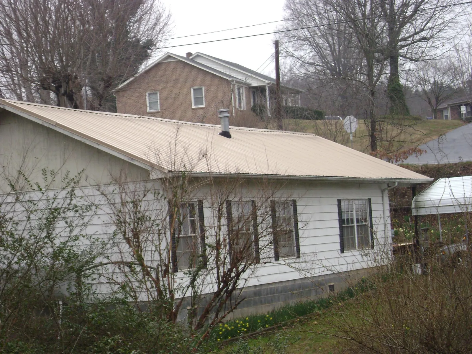 Tan metal roof on a white sided house set into a hillside — Commercial Roofing by Roofing Brothers in Inver Grove Heights